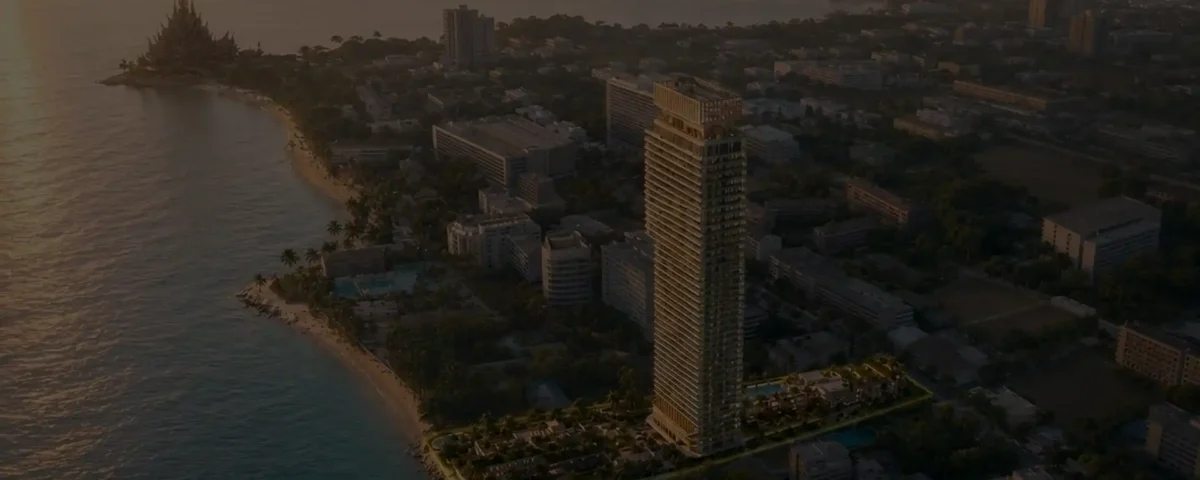 Aerial view of a coastal city at sunset featuring a tall modern high-rise near a sandy beach and palm trees along the shore.